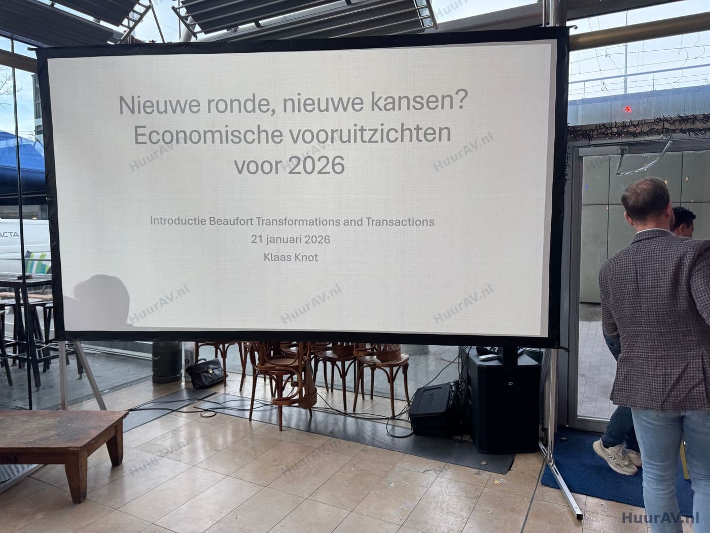 Spreker op een congrespodium in Amsterdam met een groot scherm en heldere presentatietechniek